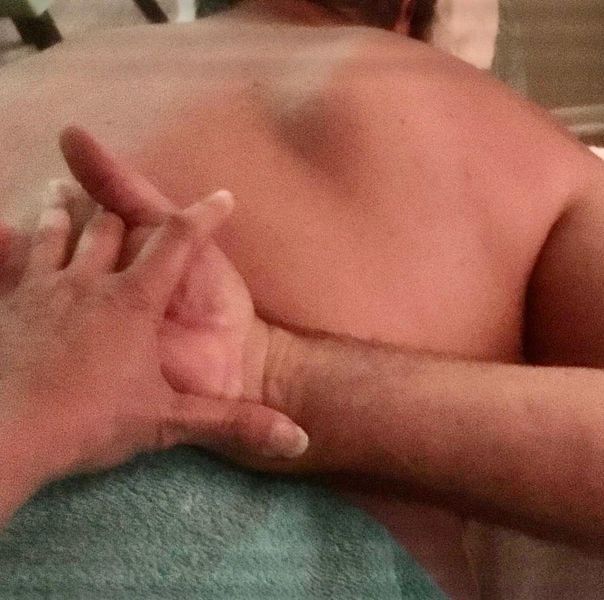 Hand massaging another's arm and shoulder, torso in frame, over blue towel.