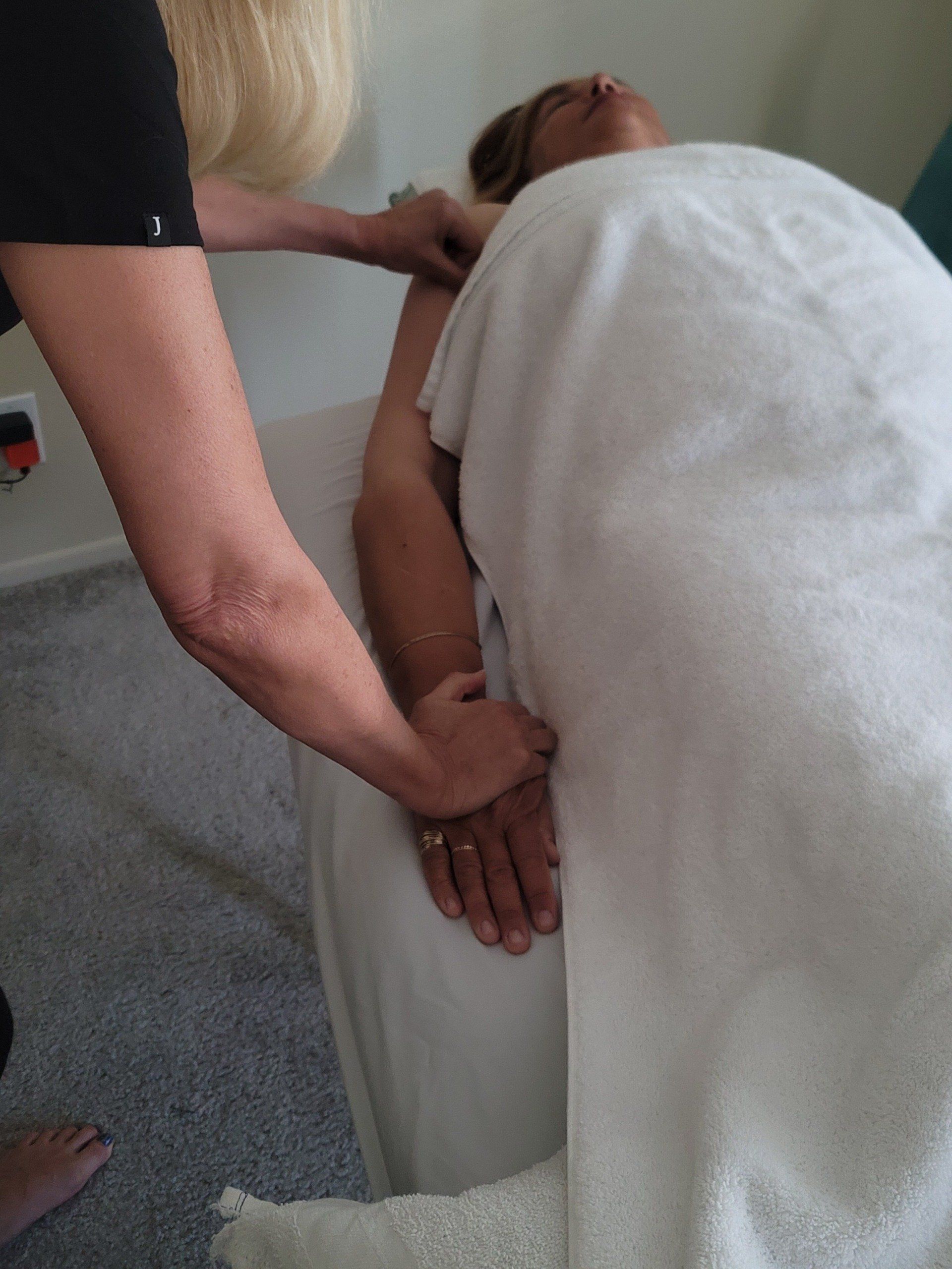 Person receiving arm massage on a massage table, covered by a white sheet.