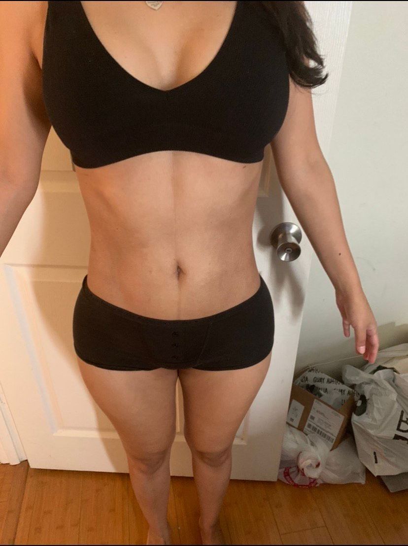 Woman in black bra and shorts standing near a door.