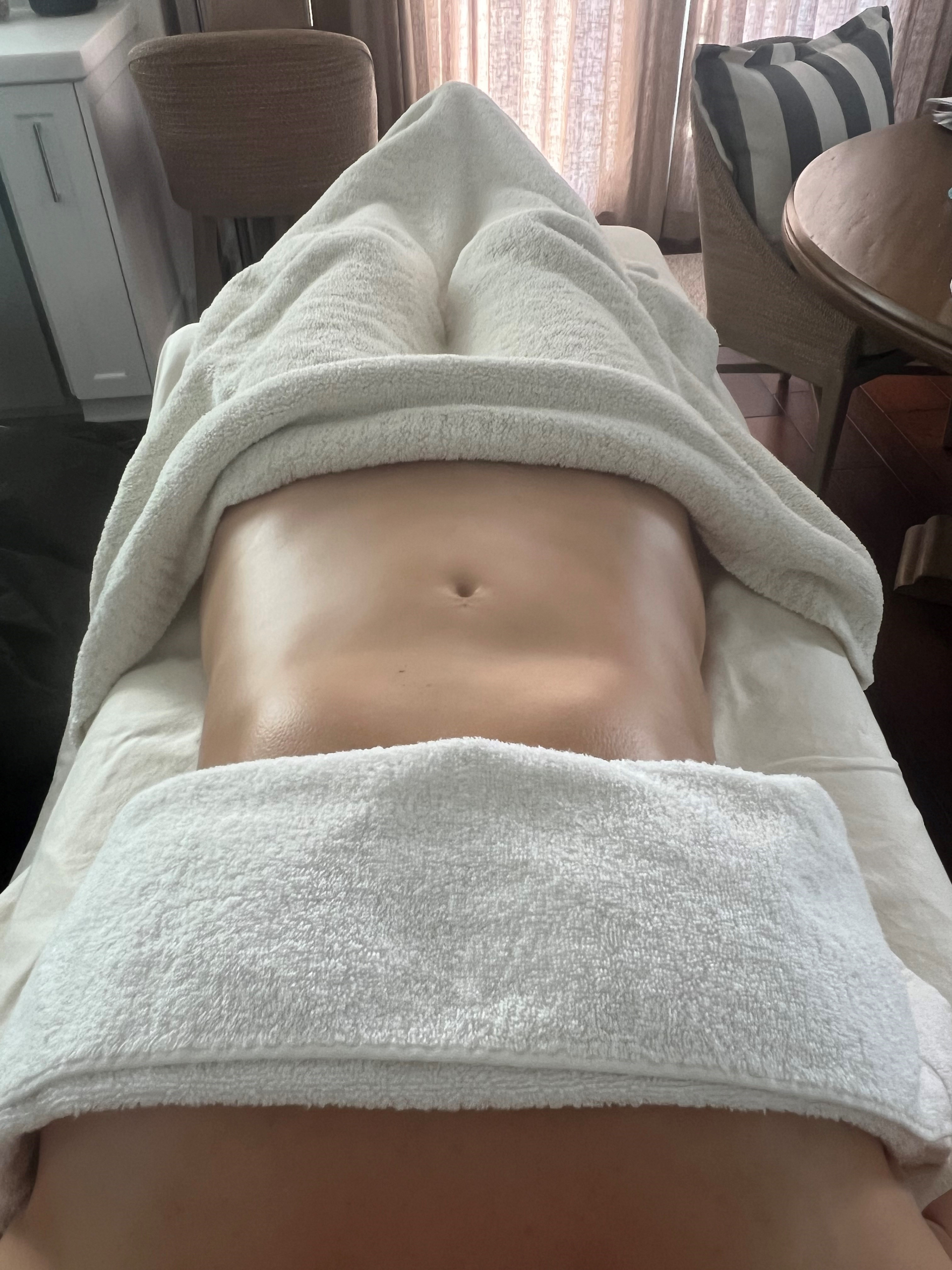 A person's abdomen, covered by white towels, on a massage table.