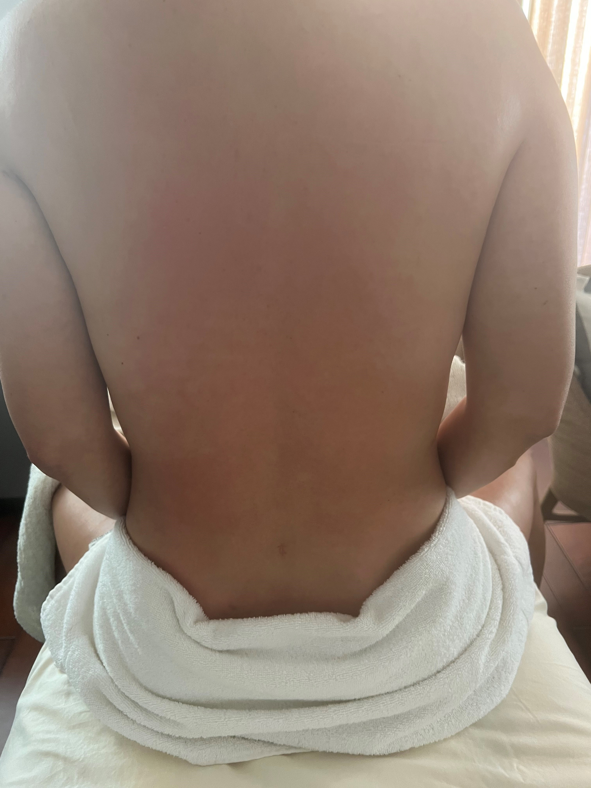 Person's bare back; wrapped in a white towel, seated. Focus on back, skin appears light.