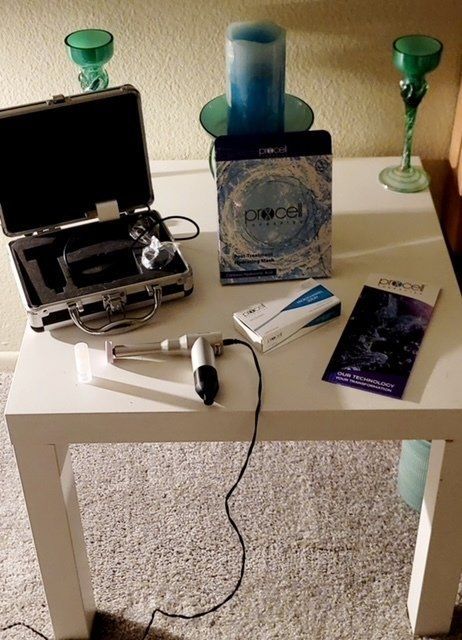 A white table with a device, case, box, and pamphlet. The device has a black cable. Two green glass candle holders are visible.