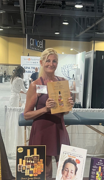 Woman holding brochure at a trade show booth, wearing a maroon dress.