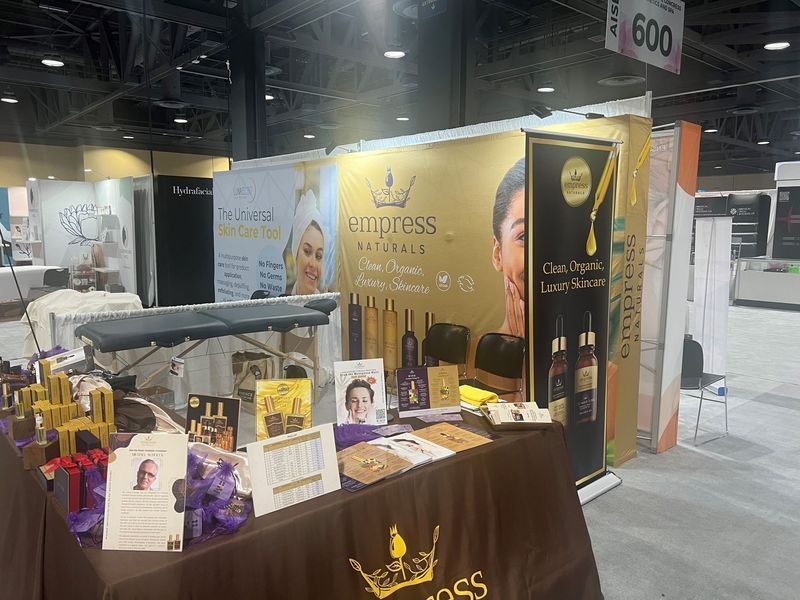 Trade show booth with skincare products and branding, featuring a table, banner, and massage table.