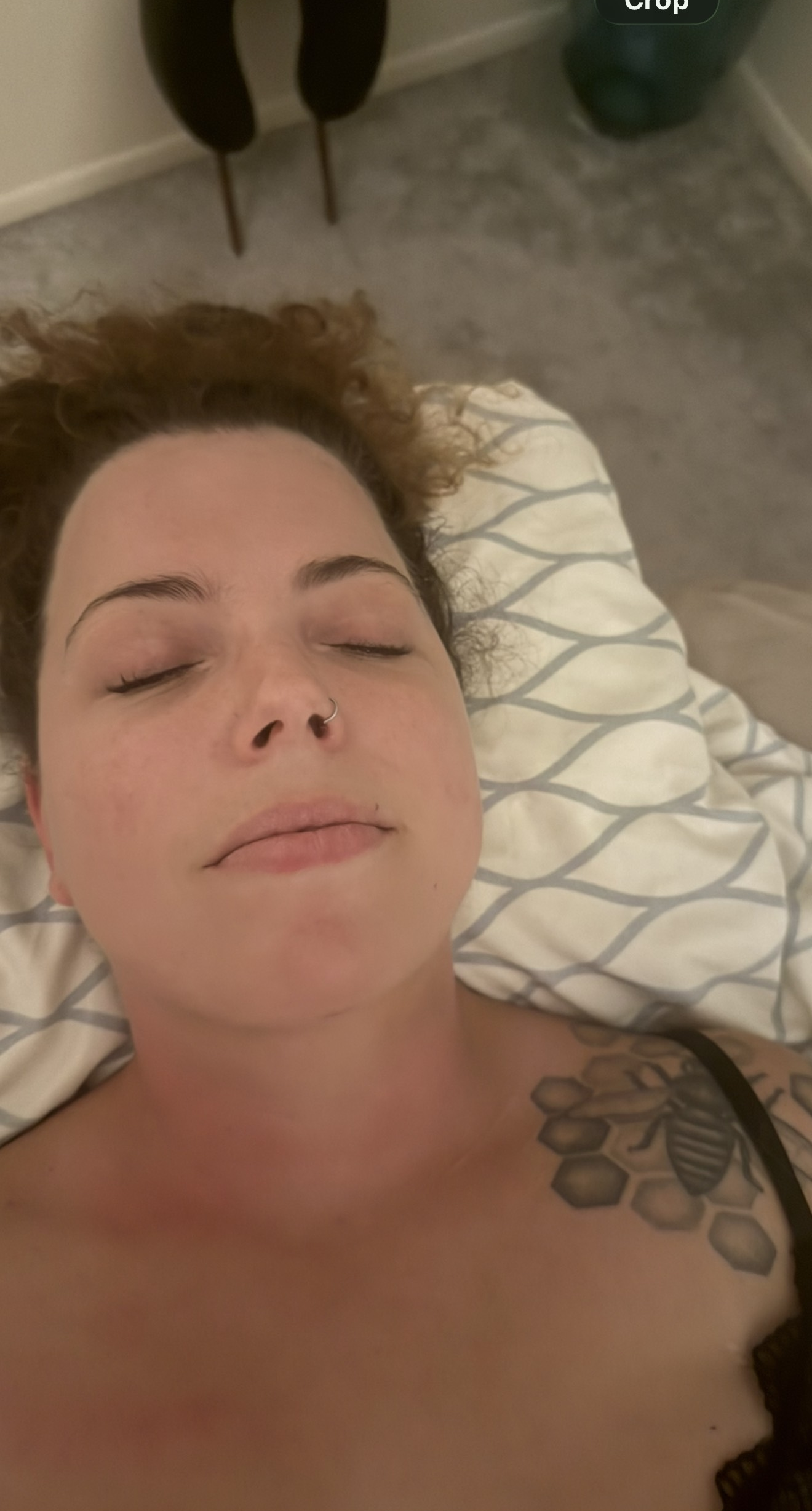 Woman lying down with eyes closed, tattoo on shoulder.