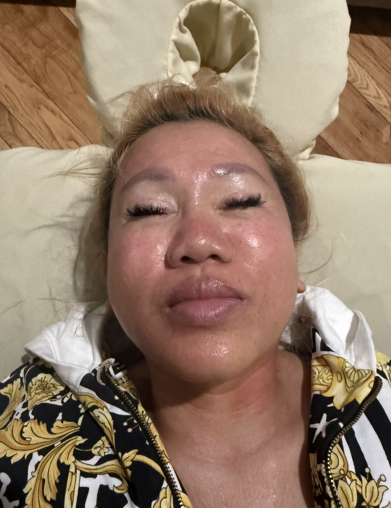 Woman with flushed face, lying down. Head on massage table with open face area. She has closed eyes.