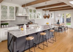 Bright modern kitchen with a marble island, black stools, white cabinets, and wood floors