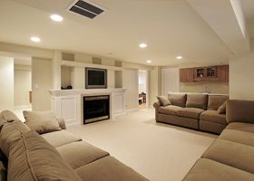 Spacious beige living room with sofas, fireplace, and TV in a bright, modern basement-style setting