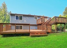 Back deck and stairs on a gray house, with a grassy yard and trees in the background