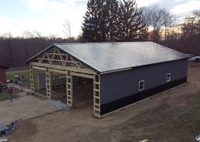 New metal-roofed barn with open front bays in a rural yard at dusk