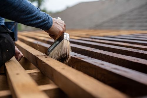 A hand brushes stain onto wooden slats on an outdoor deck