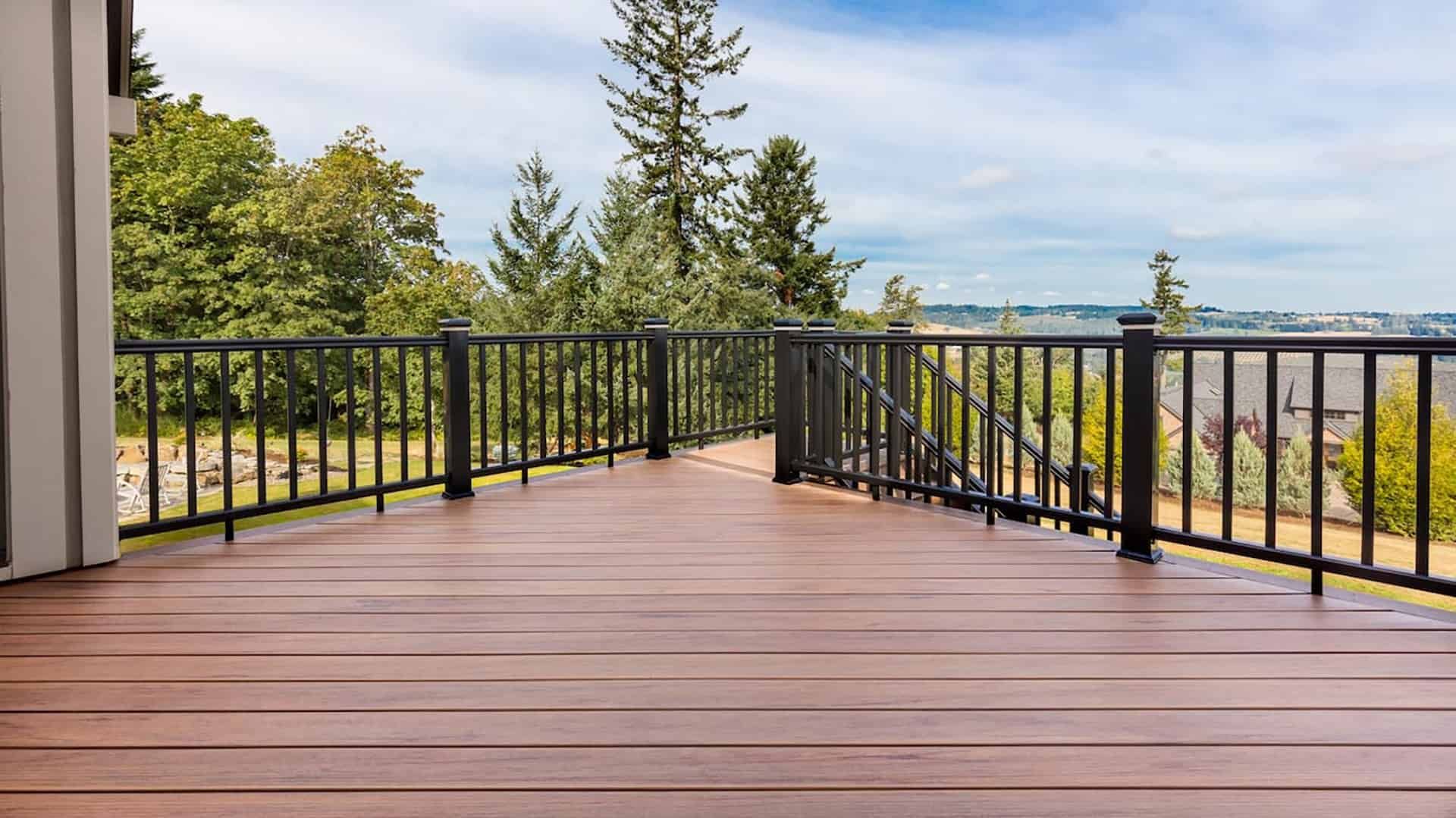 Wooden deck with black railings overlooking trees and a distant city skyline under a bright sky