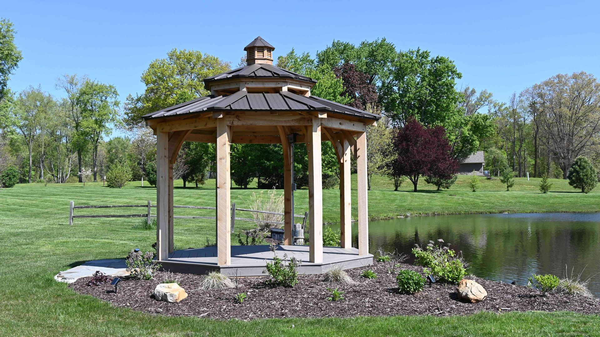 Wooden gazebo beside a pond in a green park with trees and flowers