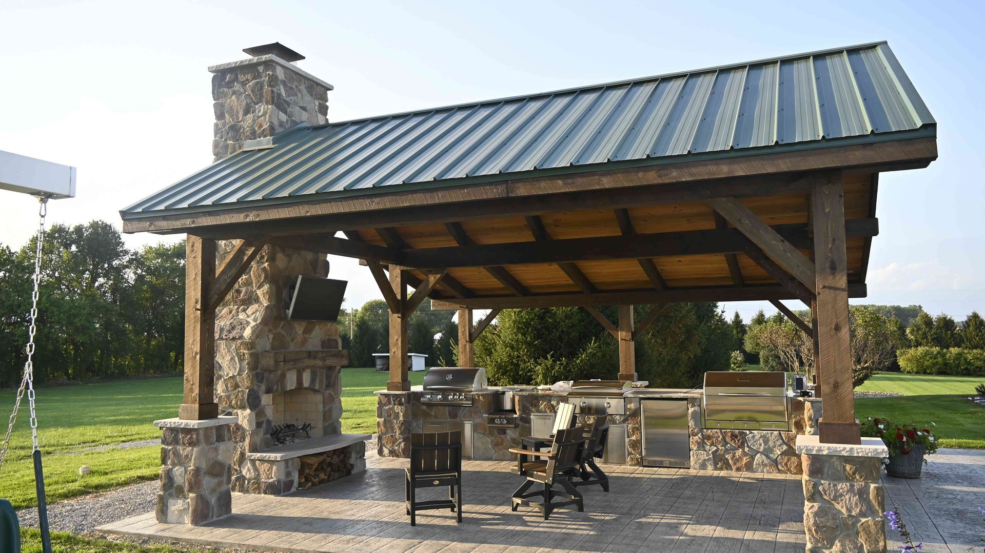 Stone and wood pavilion with metal roof and picnic tables in a sunny park