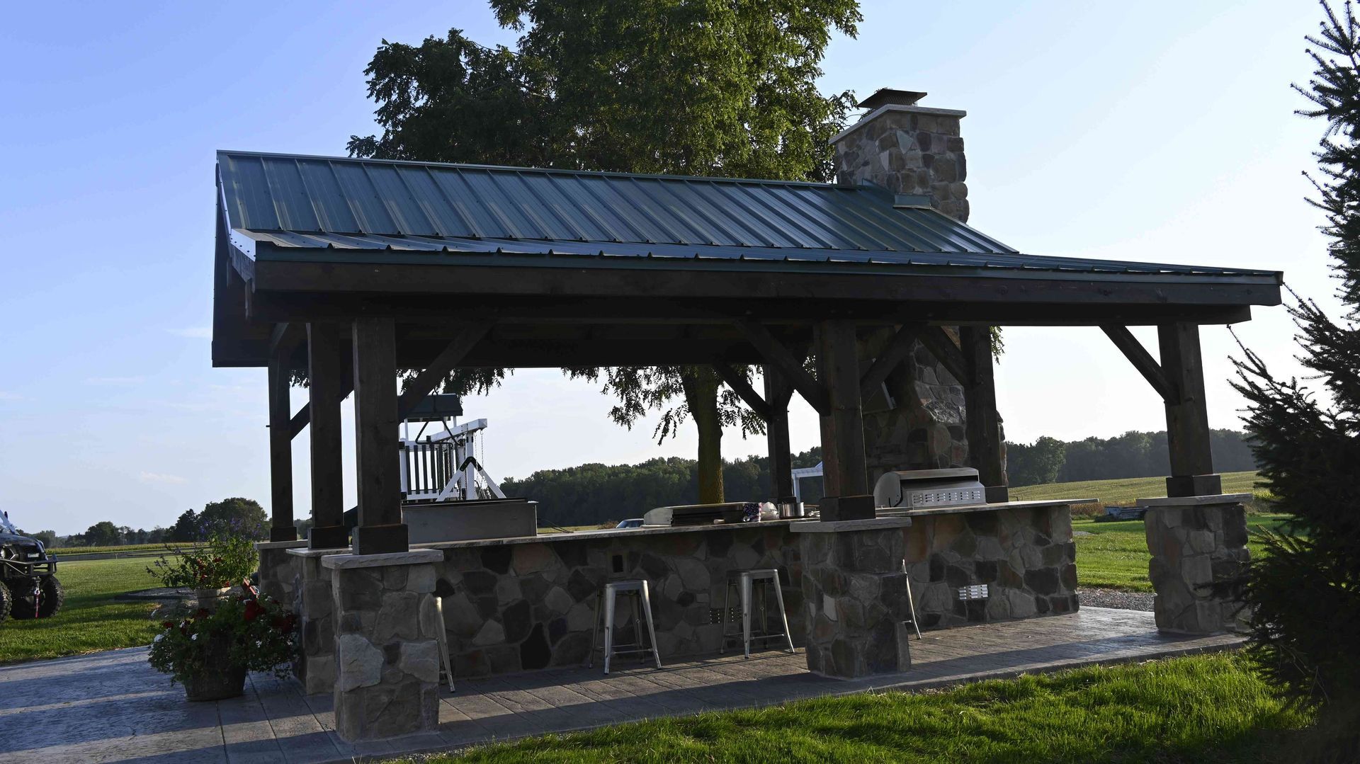 Stone pavilion with a dark metal roof in a grassy field at sunset