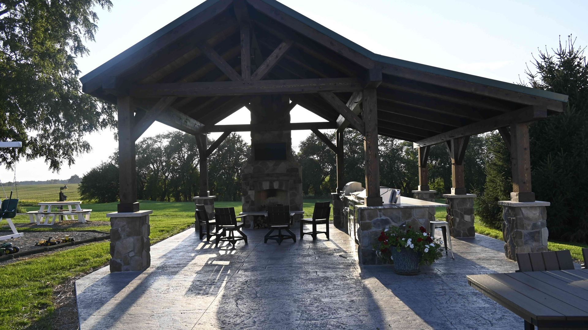 Covered outdoor pavilion with stone columns and picnic tables in a sunny park