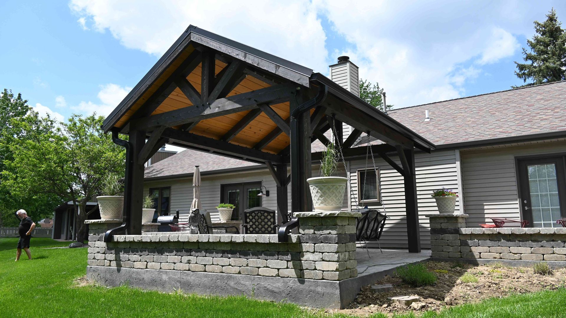 Stone house with a covered wooden porch and green lawn under a partly cloudy sky