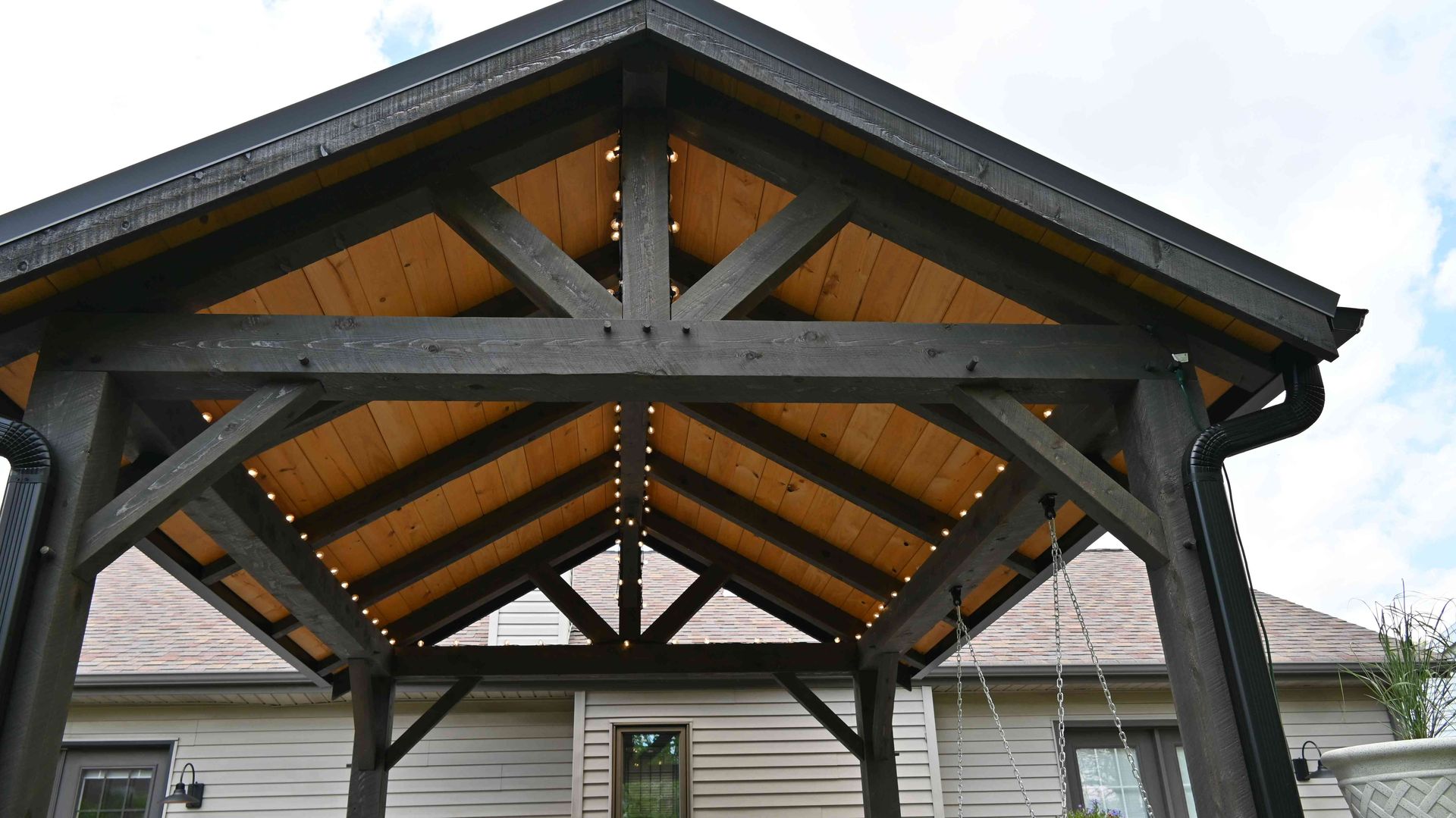 Wooden pavilion with exposed rafters and a peaked roof over a backyard or patio area