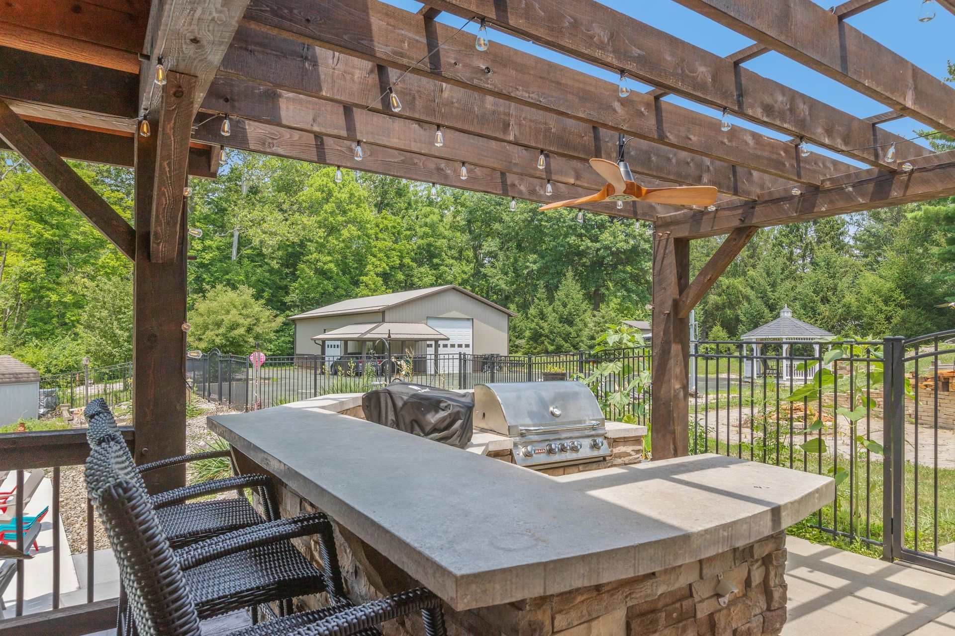 Covered patio with outdoor bar seating, stone counter, and backyard view beyond the railing