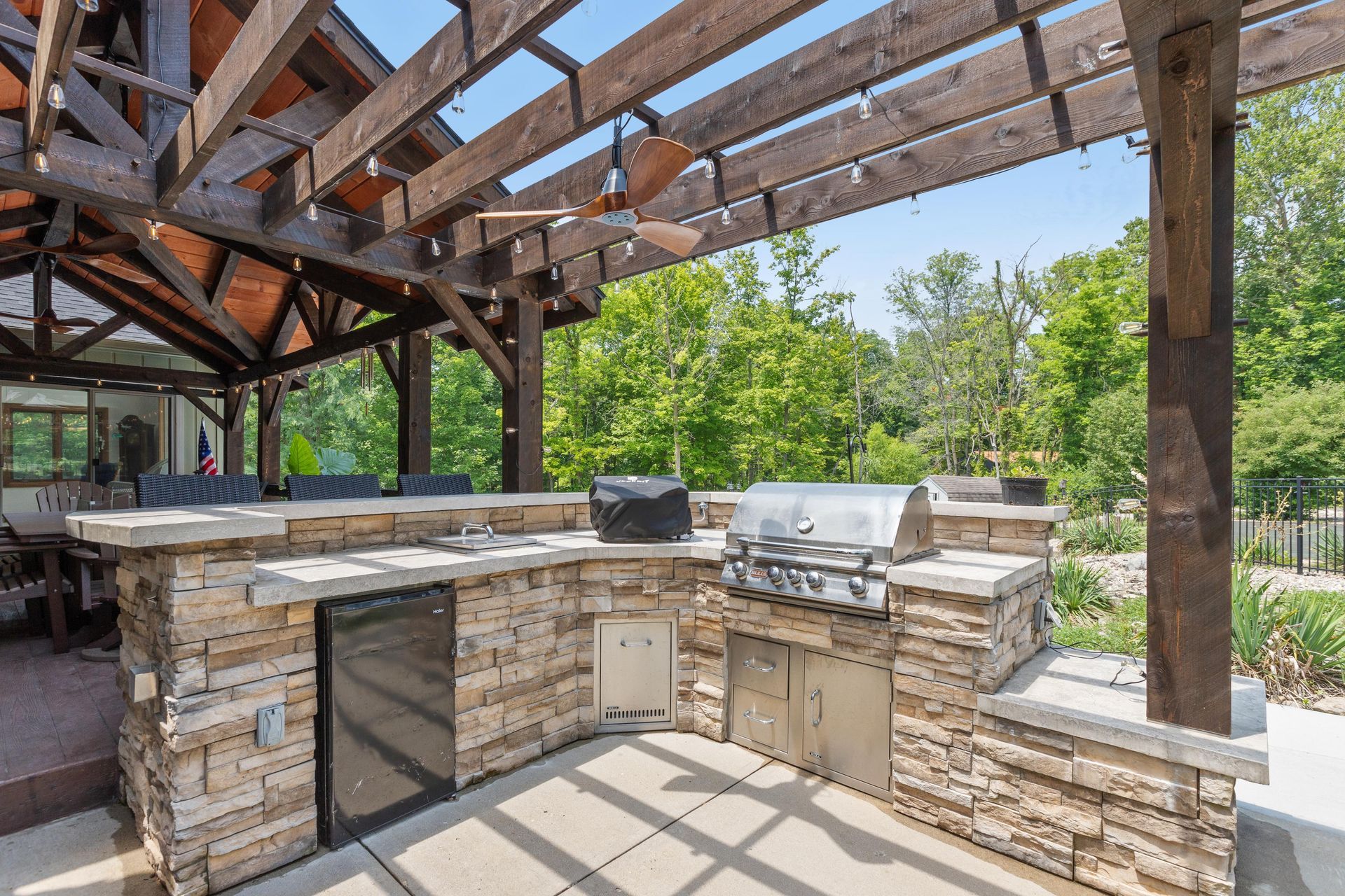 Outdoor stone kitchen with grill and sink under a wooden pergola