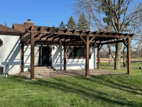 White house with wooden pergola patio in a grassy yard under a clear blue sky
