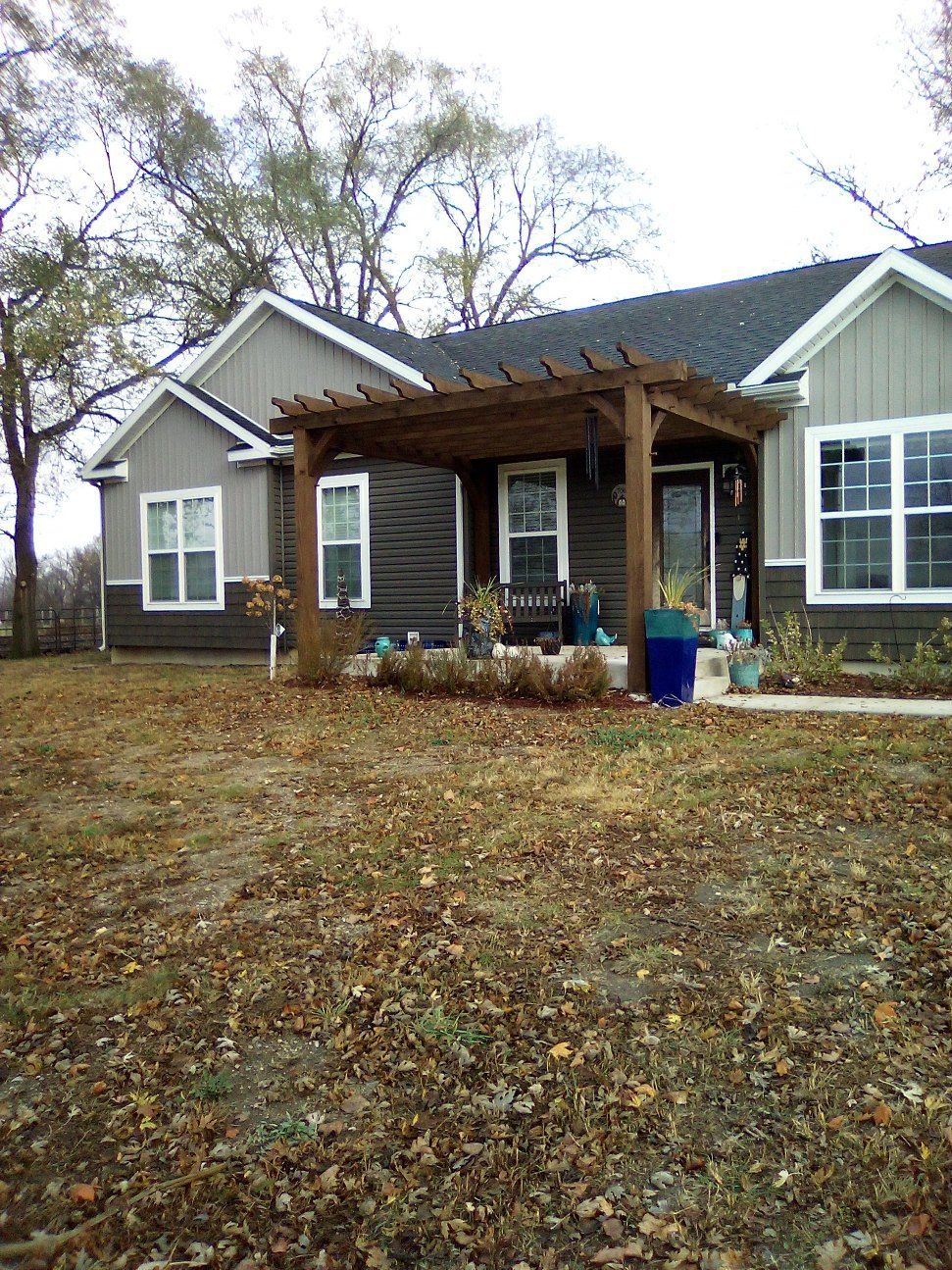 Small gray house with a wooden front porch and leaf-covered yard in autumn