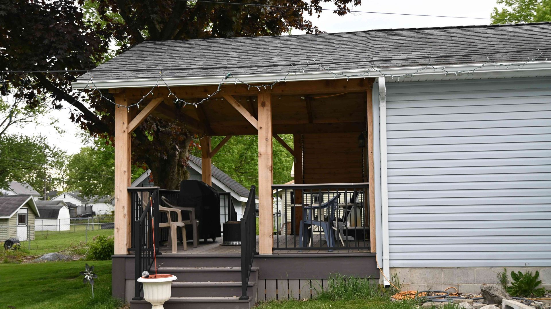 Front porch with wooden posts on a gray house, featuring steps, a chair, and a hanging planter