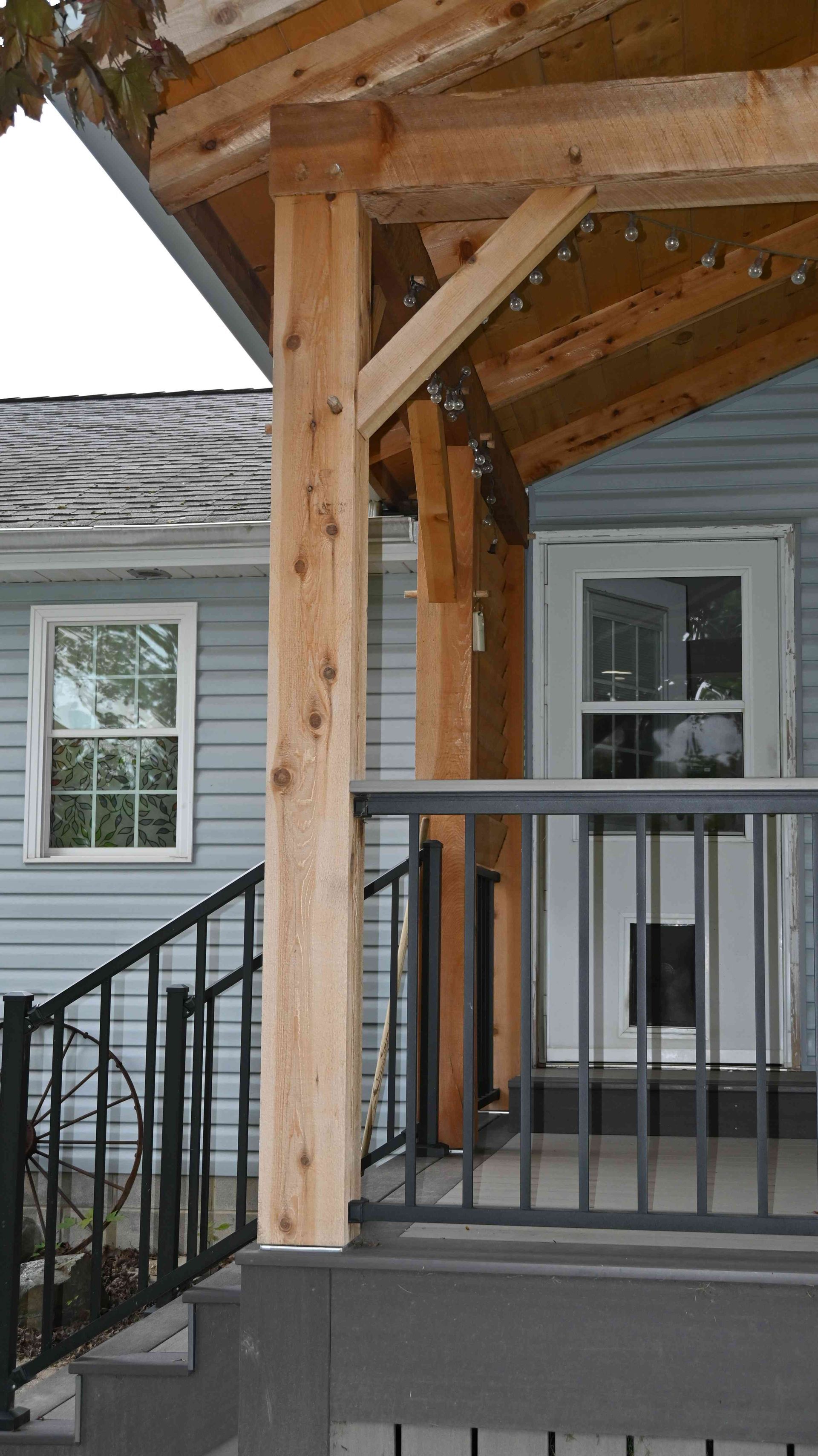 Wooden porch post and railing with roof overhang beside a gray house exterior