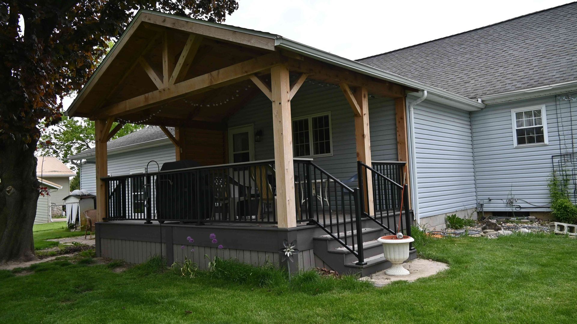 Covered porch with wooden posts and black railing on a white house, beside a grassy yard.