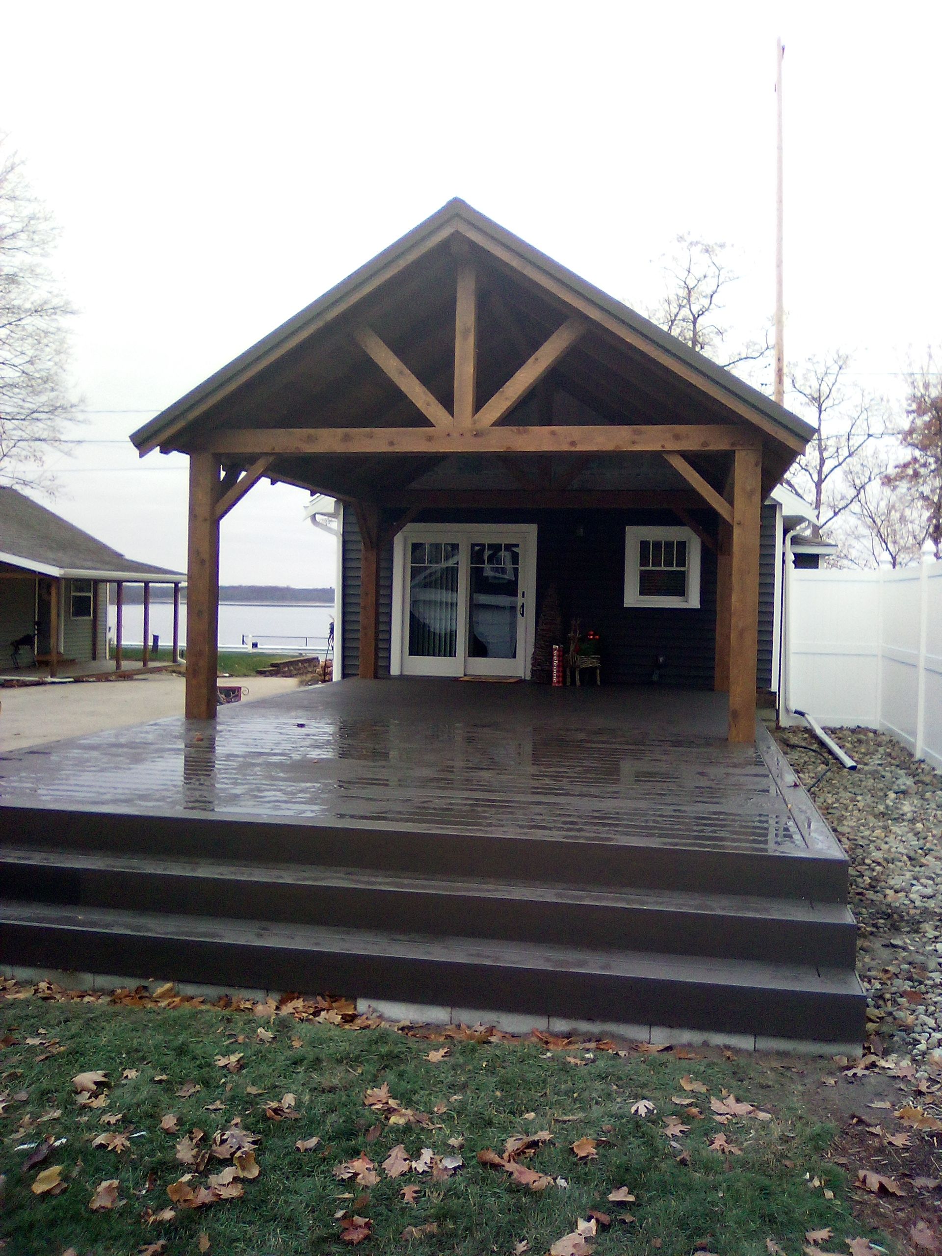 Small wooden pavilion with steps and a wet porch on a rainy day, with a glass door and windows.