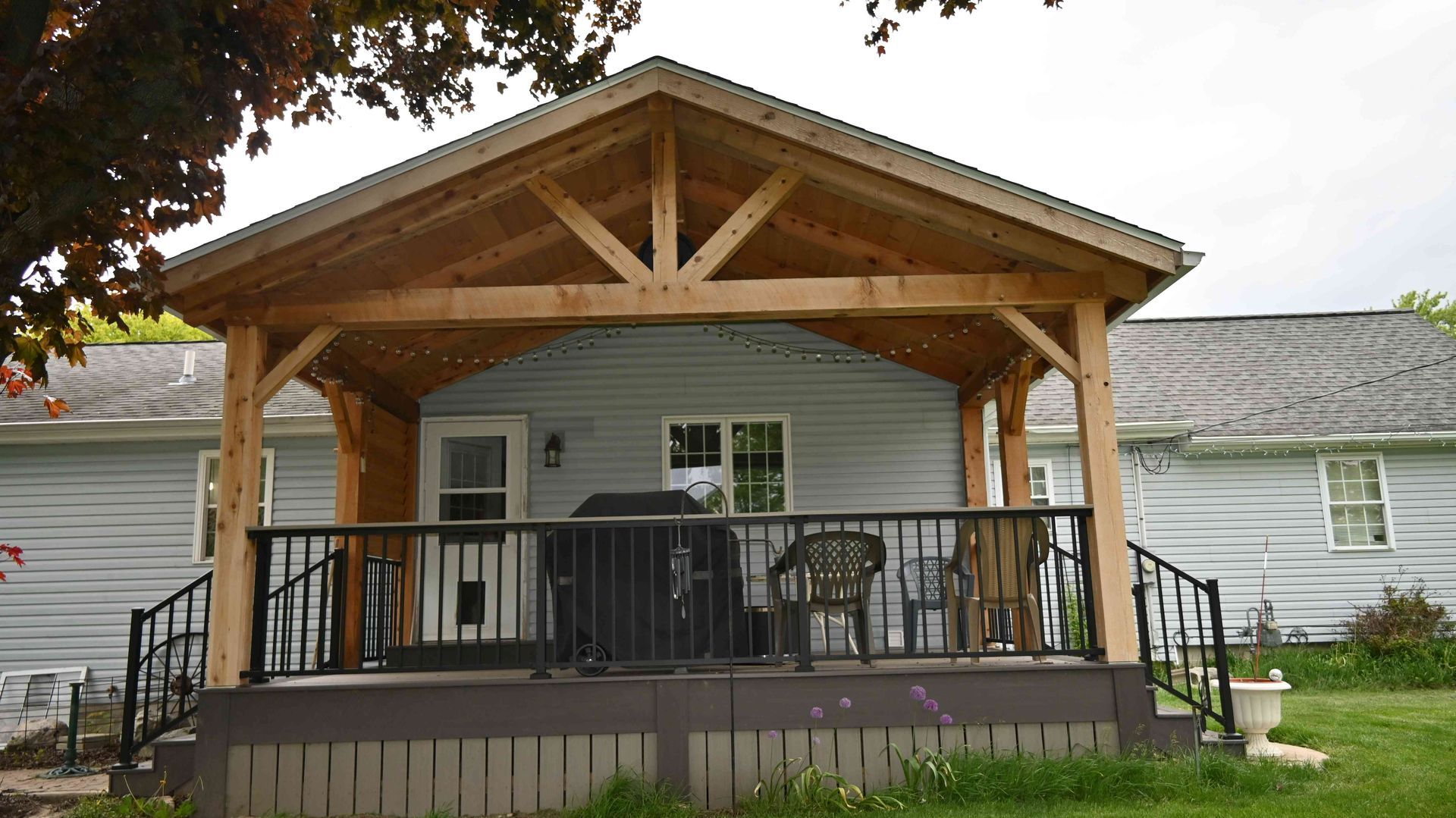 Covered front porch with wooden roof and black railing on a white house, seen from the yard.