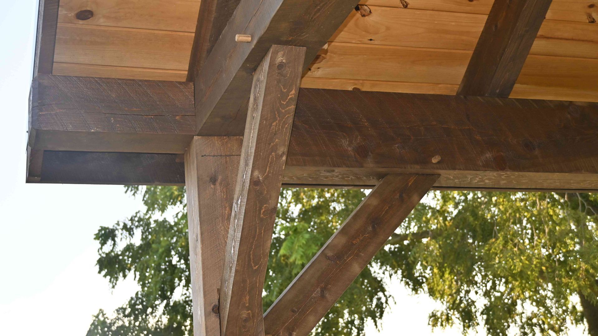 Wooden deck beam and support posts with diagonal brace under a roof, viewed from below.