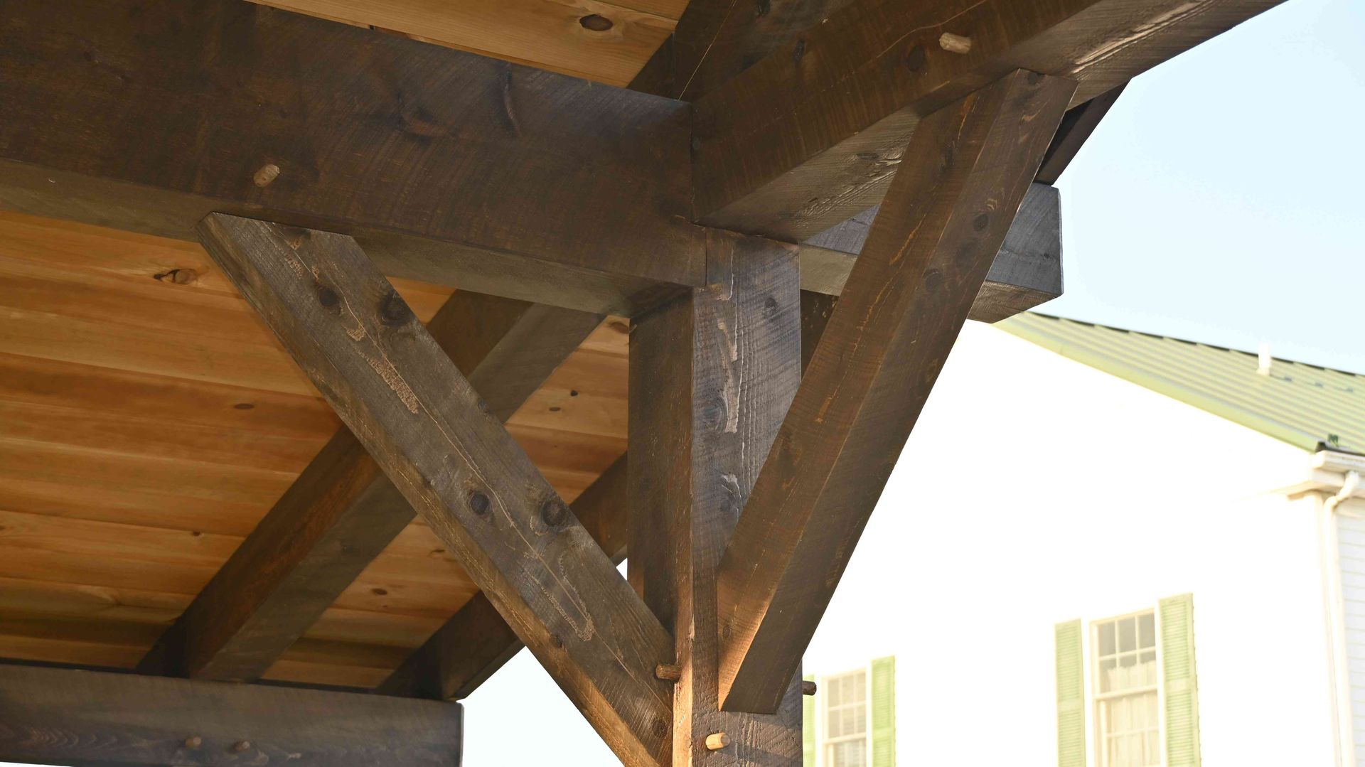 Wooden support beams under a roof overhang against a bright exterior wall