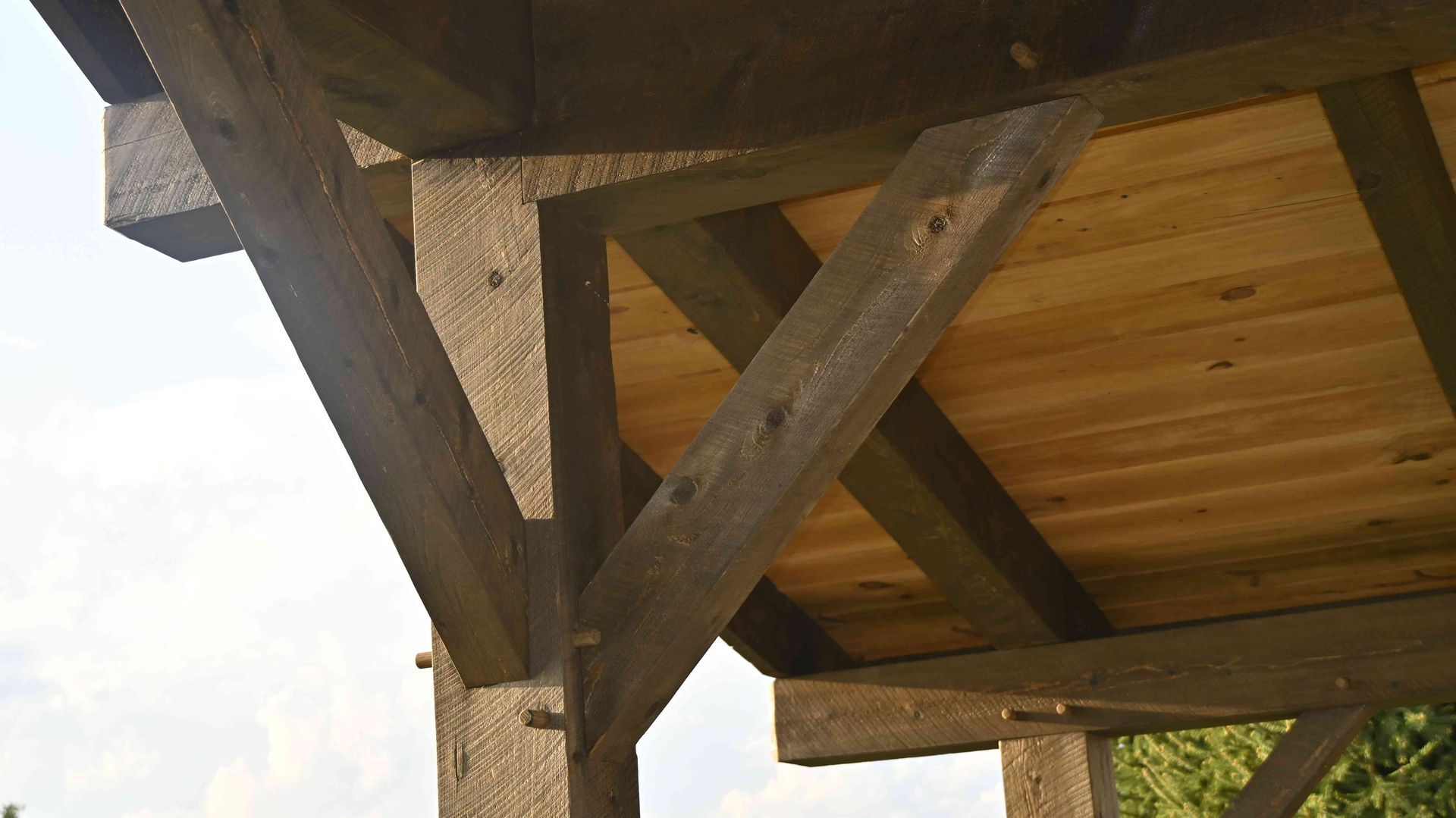 Wooden pavilion roof supported by dark timber beams and posts against the sky