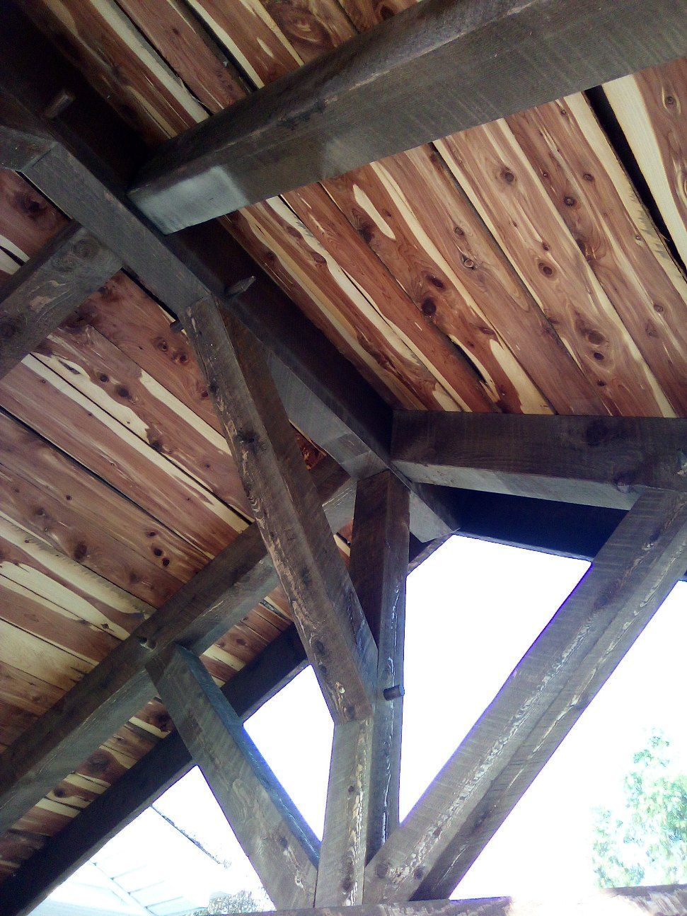Wooden roof beams and weathered planks viewed from below, with daylight showing through gaps