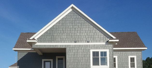 Front of a gray house with white trim and a steep gabled roof under a blue sky
