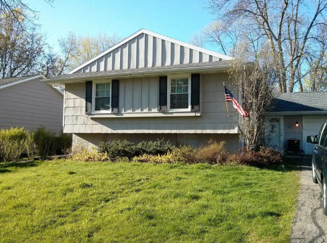 Suburban house with beige siding, green lawn, and an American flag by the front window