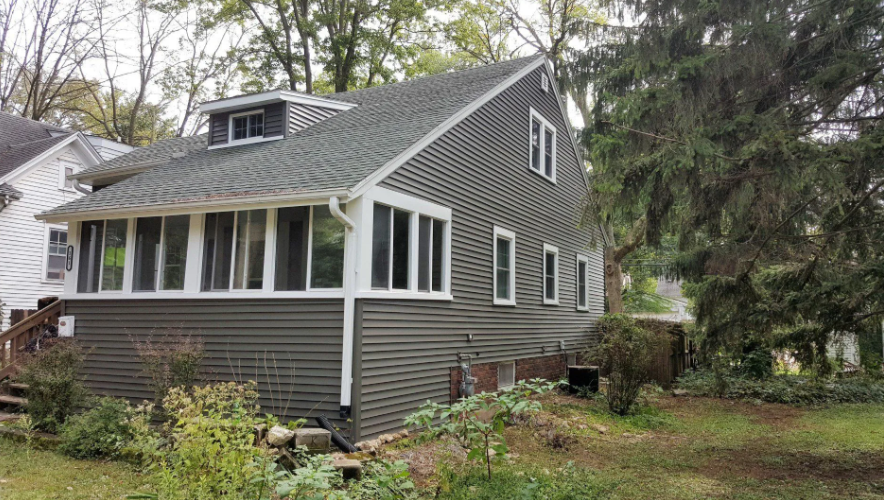 Gray two-story house with white trim and porch, surrounded by trees and a grassy yard