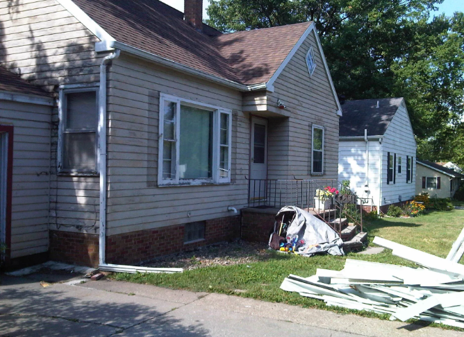 Damaged house exterior with debris and broken siding in the yard