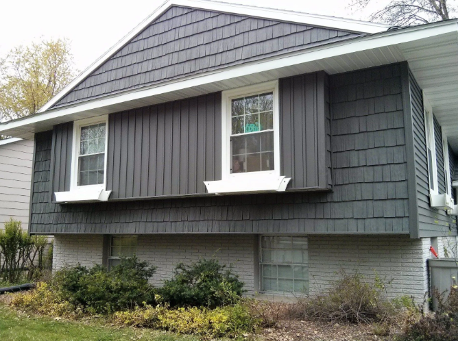Small gray house with dark shutters and a raised foundation, seen from the side.