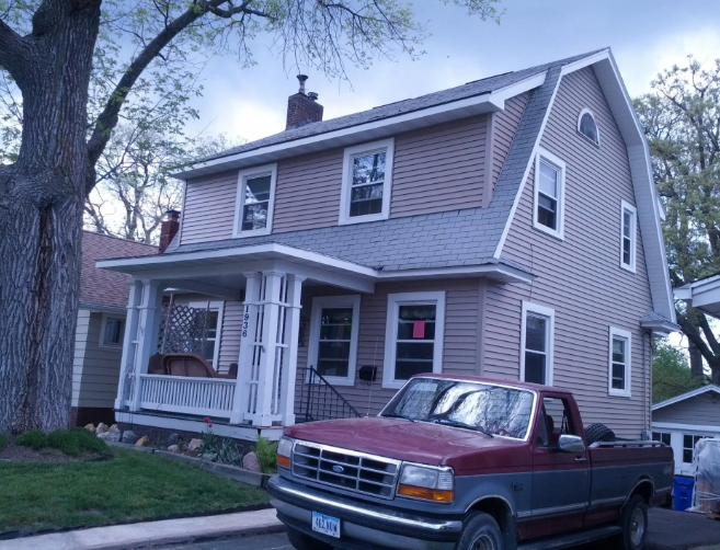 Two-story beige house with a front porch and a red pickup truck parked in front at dusk