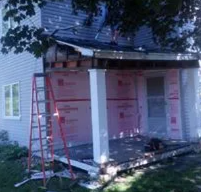 House under renovation with white foam board siding, red ladder, and porch columns visible