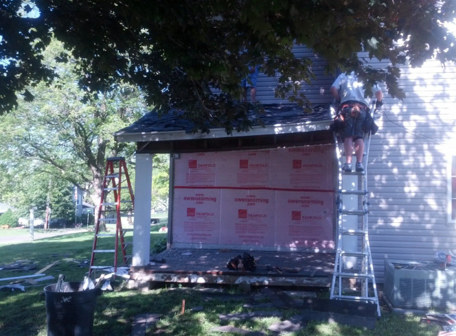 Workers on ladders installing white siding on a house under renovation in a leafy yard