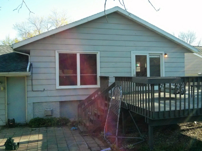 Gray house exterior with a wooden deck and patio, seen from the backyard.