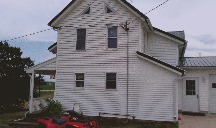 White two-story house with small porch, black shutters, and a red lawn mower in front yard