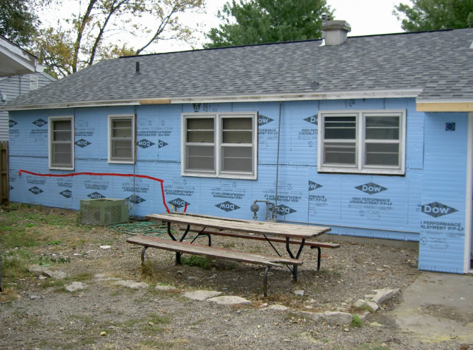 Blue house exterior with windows, construction wrap, and a picnic table in front