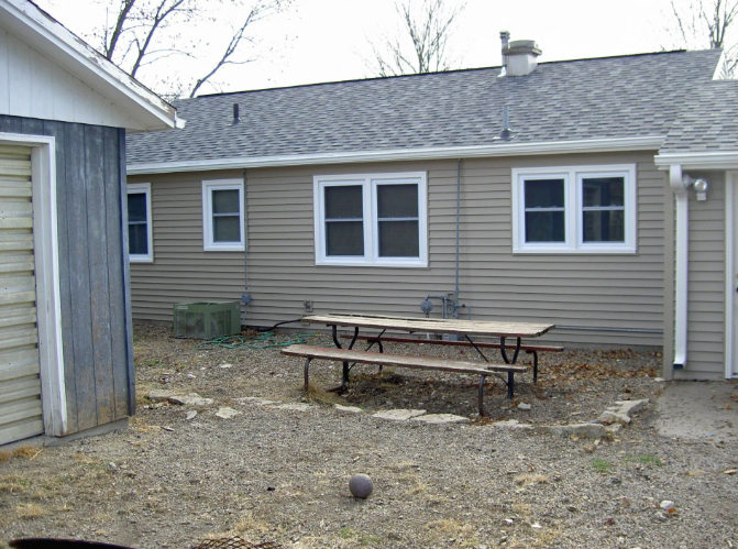 Backyard patio with picnic table beside a beige house and shed on a cloudy day