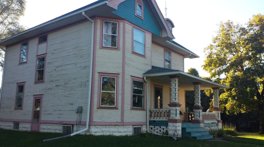 Pink house with a front porch, white trim, and trees in the yard at sunset