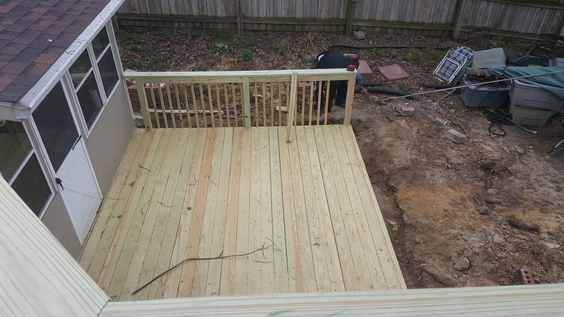 Freshly built wooden deck in a backyard beside a house, overlooking a dirt area and fence.