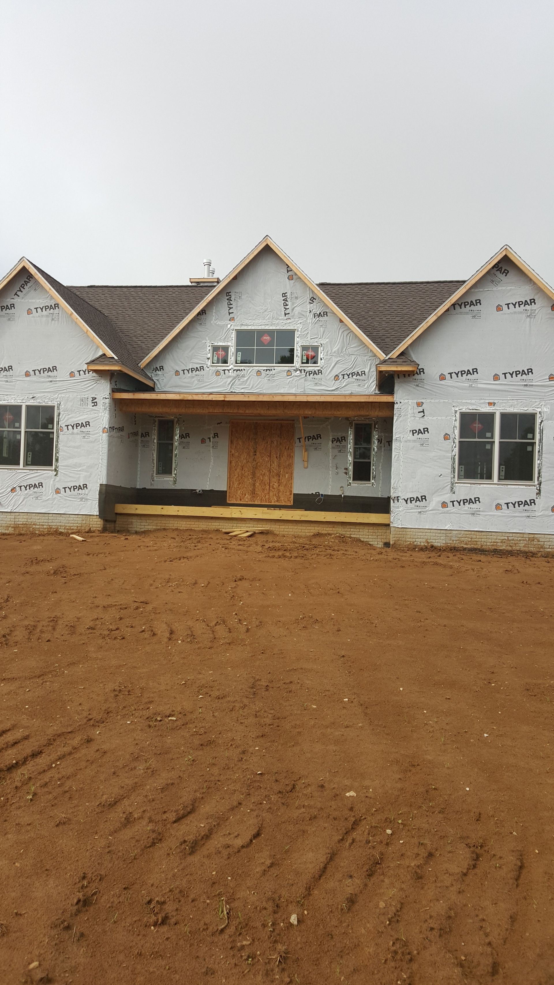 Partially built white house with gabled roofs and exposed dirt front yard